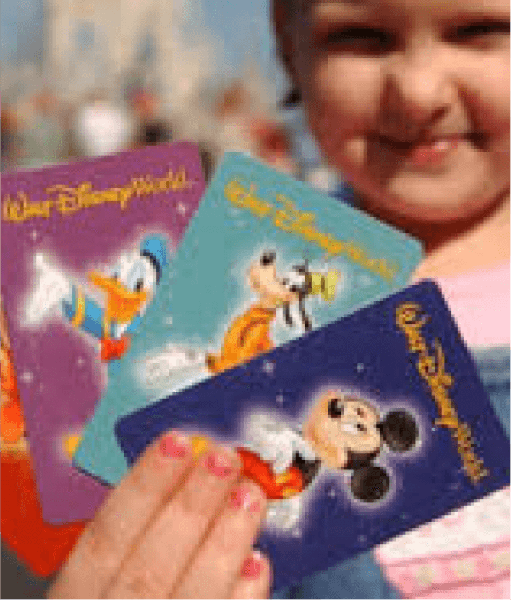 A child holds three colorful Walt Disney World cards featuring Donald Duck, Goofy, and Mickey Mouse, smiling in the background with a blurred outdoor setting.