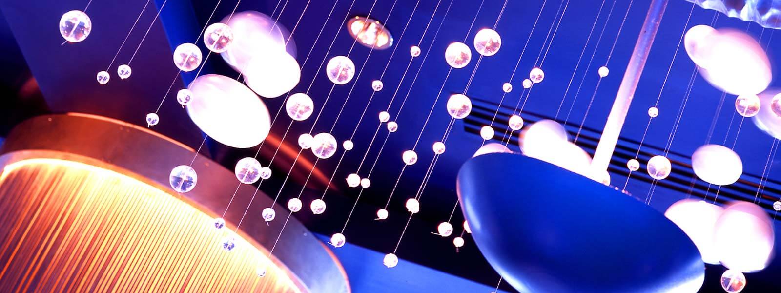 Hanging glass orbs and round lights suspended from the ceiling, illuminated with purple and blue lighting, creating a modern and artistic ambiance.