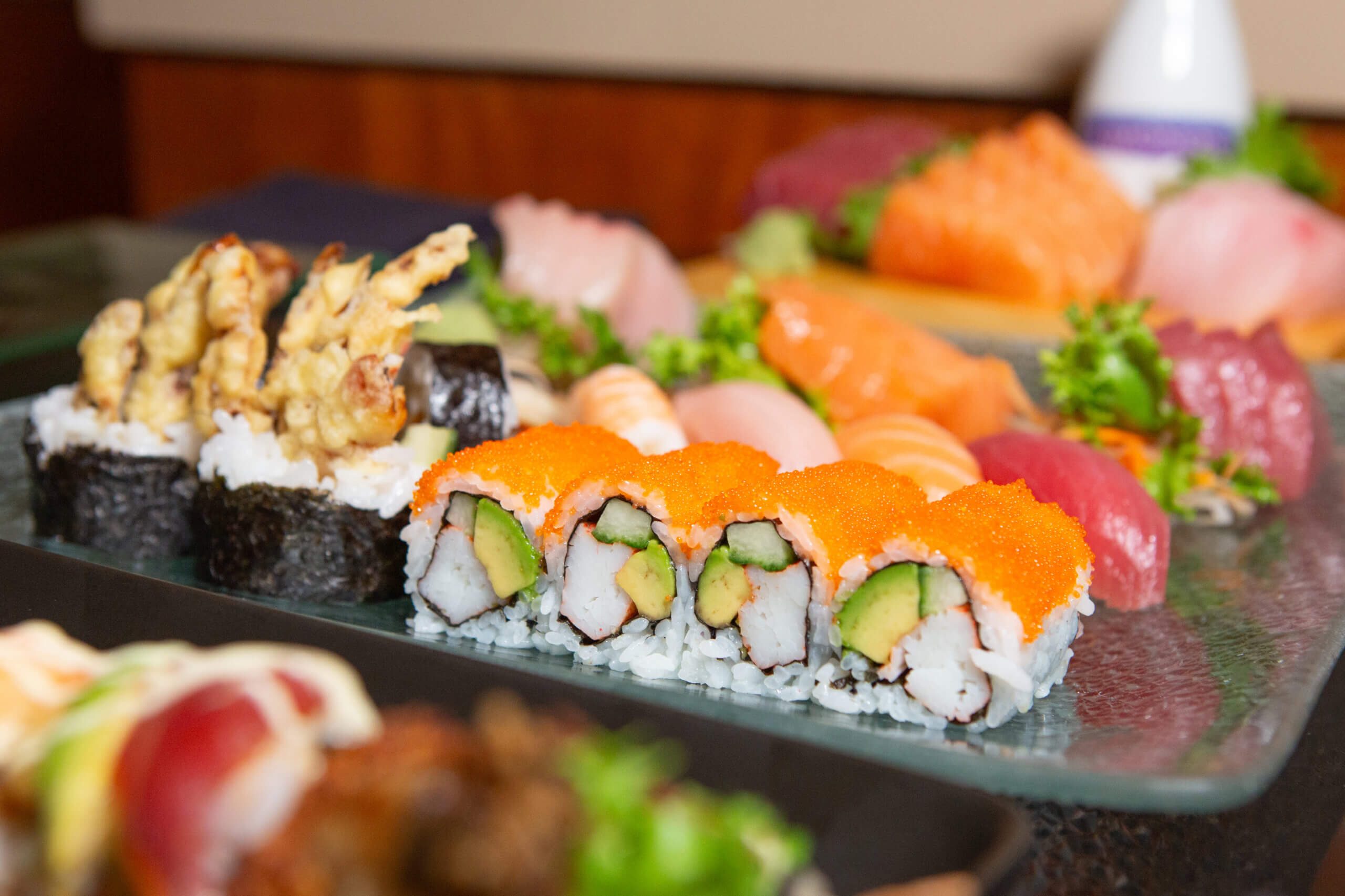A close-up of assorted sushi rolls and sashimi on a platter, featuring sushi rolls with orange fish roe, avocado, and crab, along with pieces of nigiri and sashimi garnished with greens.