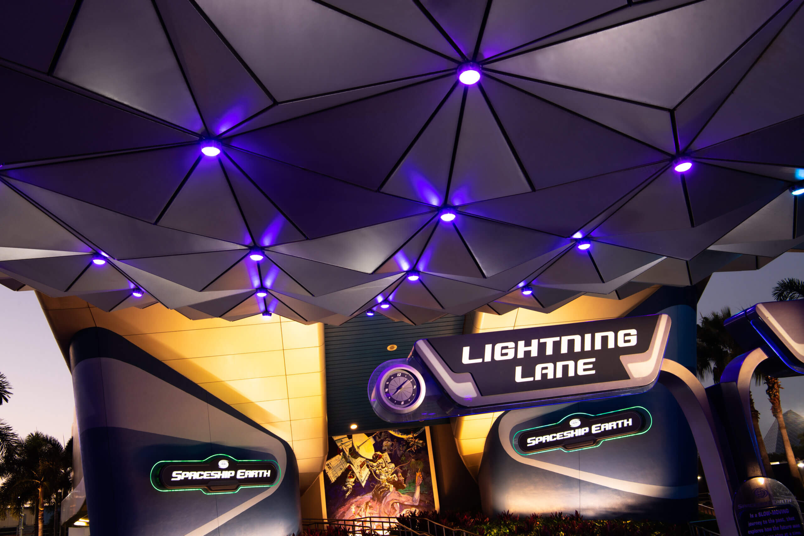 The entrance to the Spaceship Earth attraction at Epcot, featuring geometric panels above and illuminated signs that read “Lightning Lane” and “Spaceship Earth,” with purple lighting accentuating the structure.