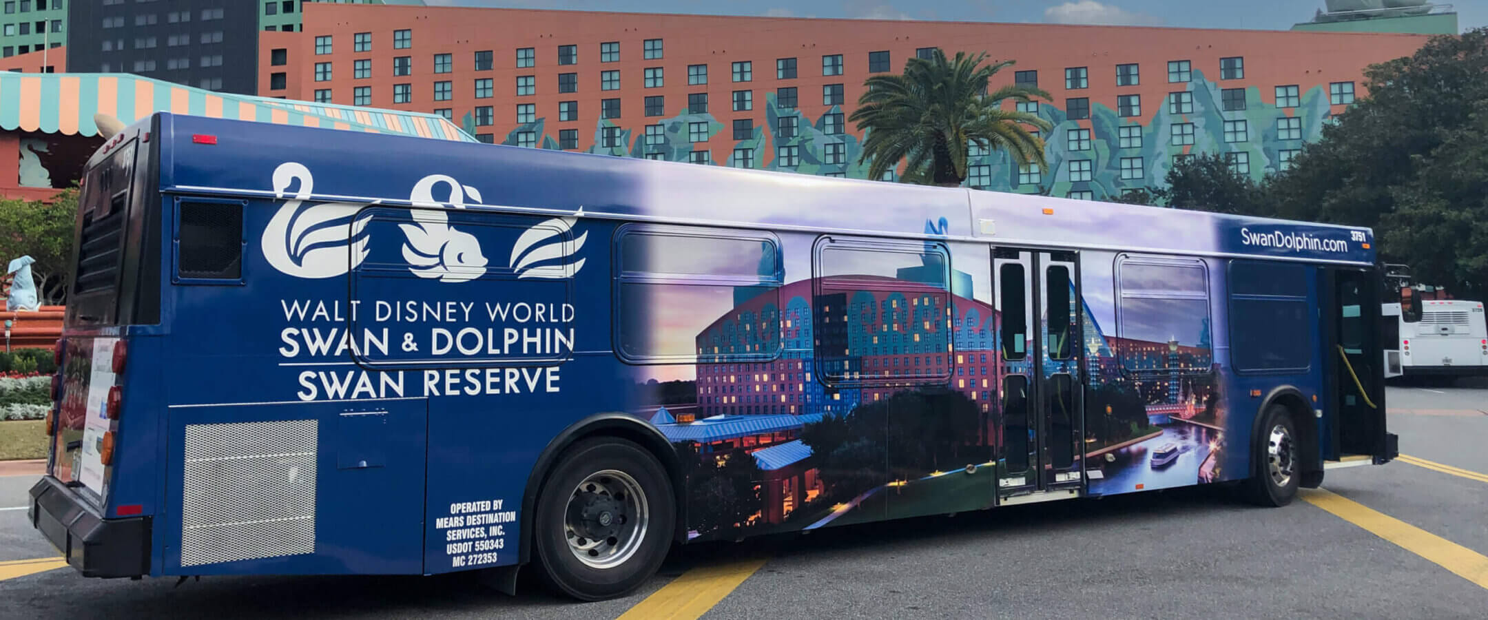 A blue bus featuring an ad for the Walt Disney World Swan & Dolphin Swan Reserve, with images of swans, hotel buildings, and the website SwanDolphin.com, parked near the resort.