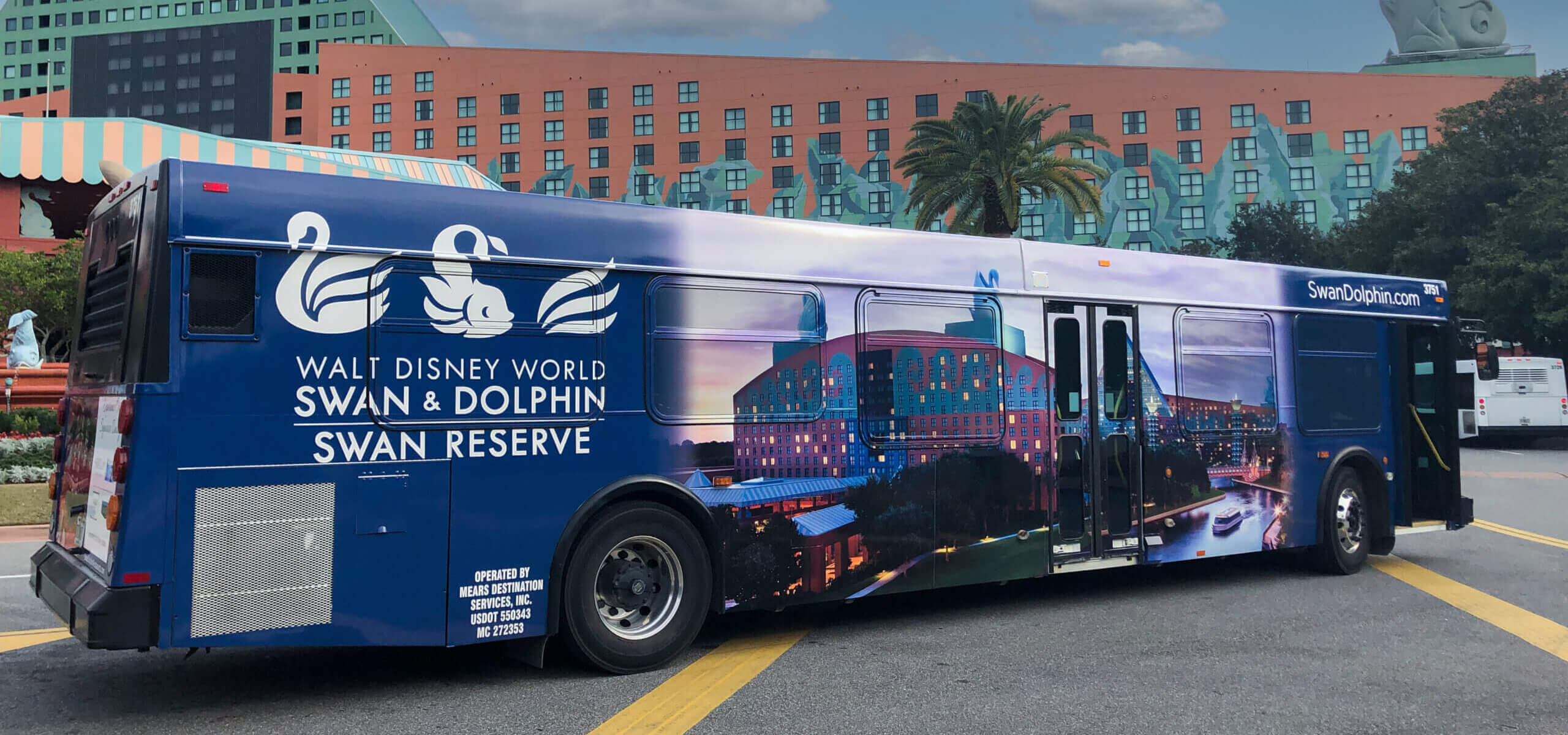 A blue bus featuring an ad for the Walt Disney World Swan & Dolphin Swan Reserve, with images of swans, hotel buildings, and the website SwanDolphin.com, parked near the resort.