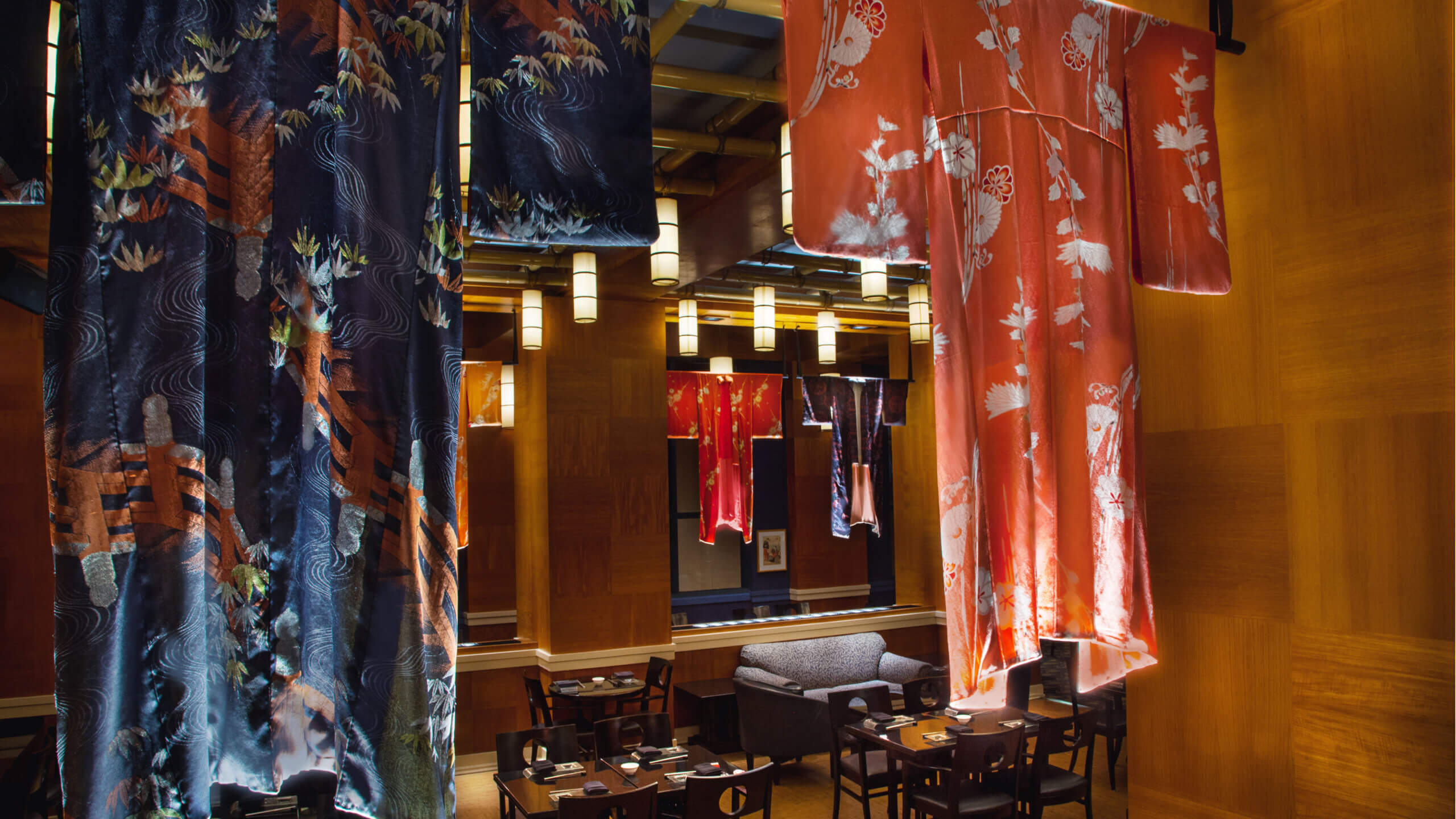 这家灯光温馨的餐厅里，色彩斑斓的kimonos 吊灯从天花板垂挂在餐桌和椅子上方，木质墙面营造出温馨的氛围，头顶还悬挂着现代风格的吊灯。