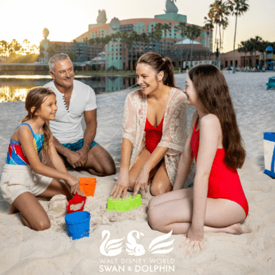 A family of four smiles and builds sandcastles together on a beach at sunset, with the Walt Disney World Swan and Dolphin Resort in the background. The resort’s logo is displayed at the bottom of the image.