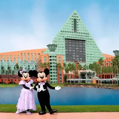 يقف ميكي وميني ماوس، وهما يرتديان ملابس رسمية، أمام فندق كبير باللونين البرتقالي والأخضر ذي سقف هرمي الشكل، محاطًا بأشجار النخيل وبركة مائية تحت سماء زرقاء.