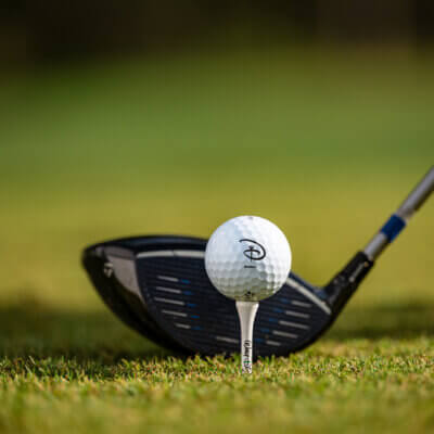 Close-up of a golf club about to hit a golf ball placed on a tee, set on green grass with a blurred background.