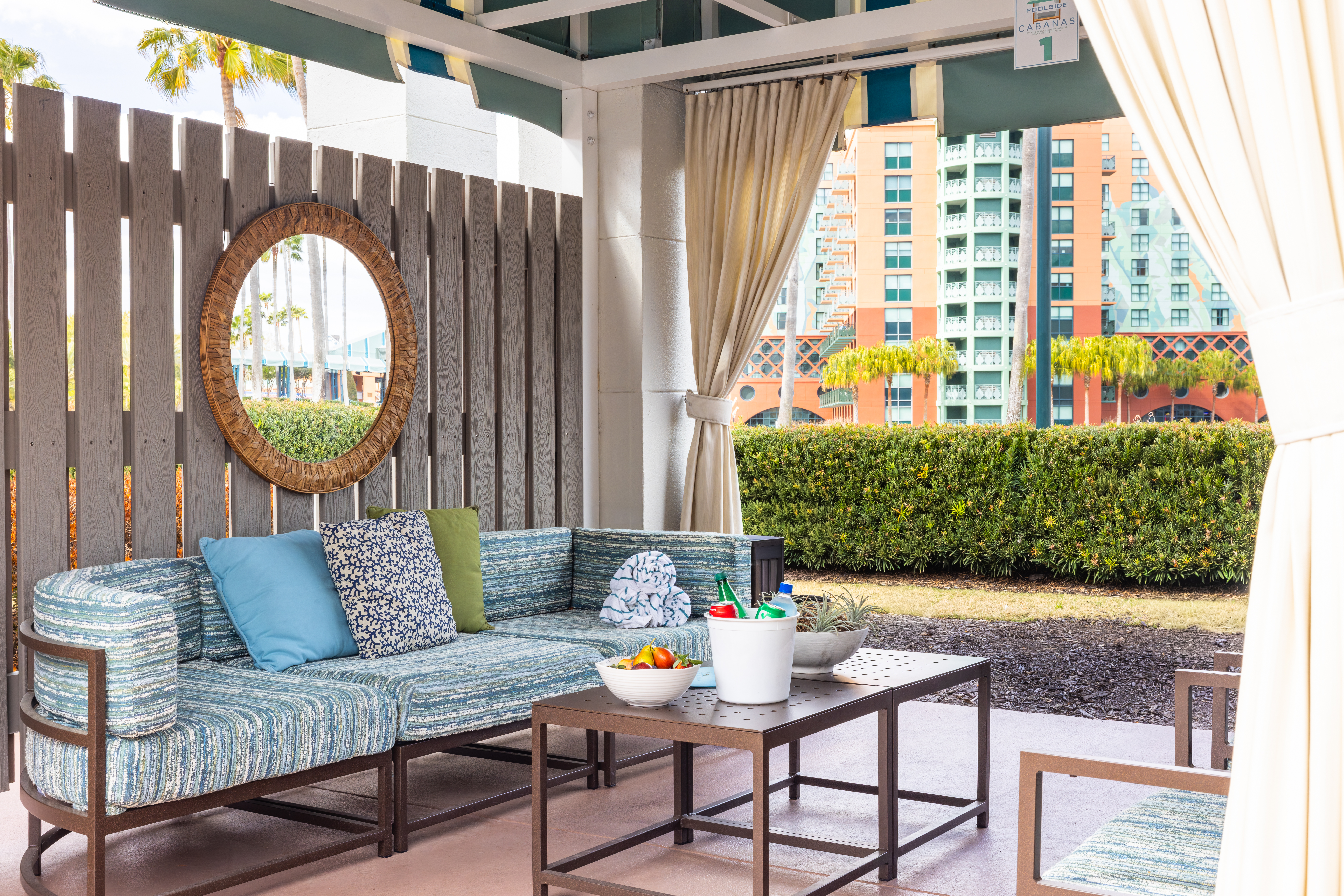 A cabana with a blue couch mirror, towels and fruit and water on the table.