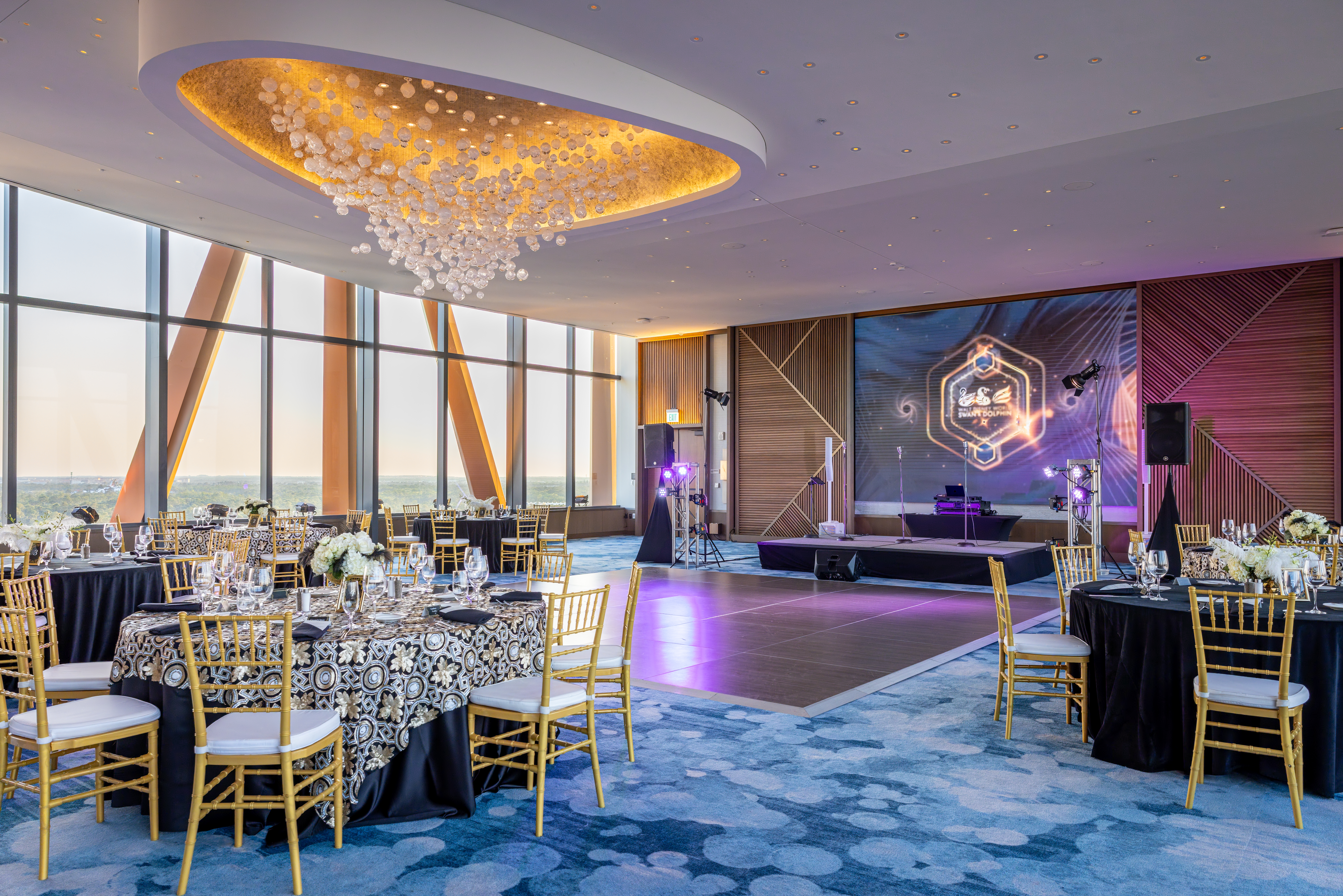 Meeting room with blue carpet, purple lighting and a bubble chandelier, with tables and chairs set up around a stage.