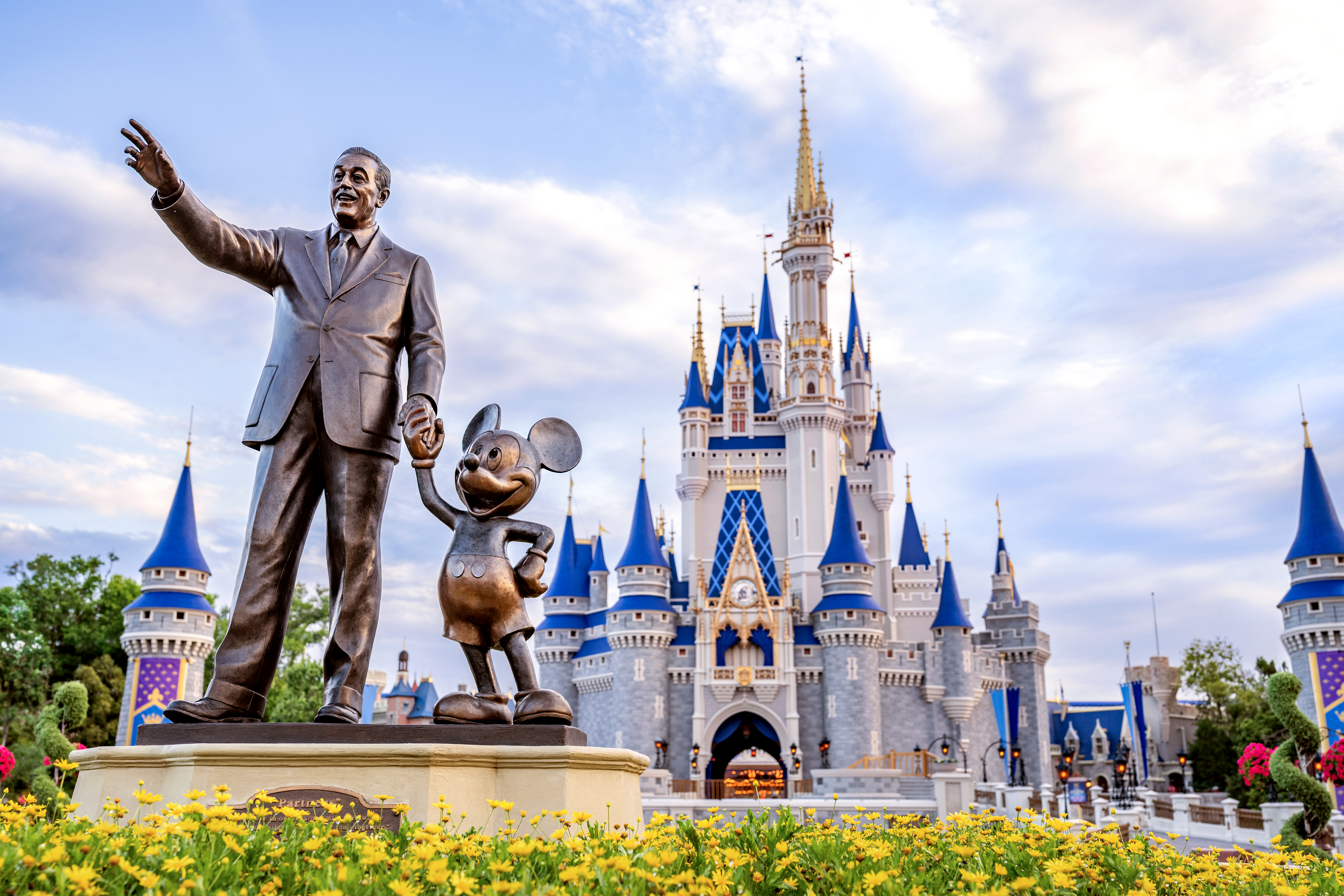 Bronze statue of Walt Disney holding Mickey's hand, with Cinderella's Castle behind them.