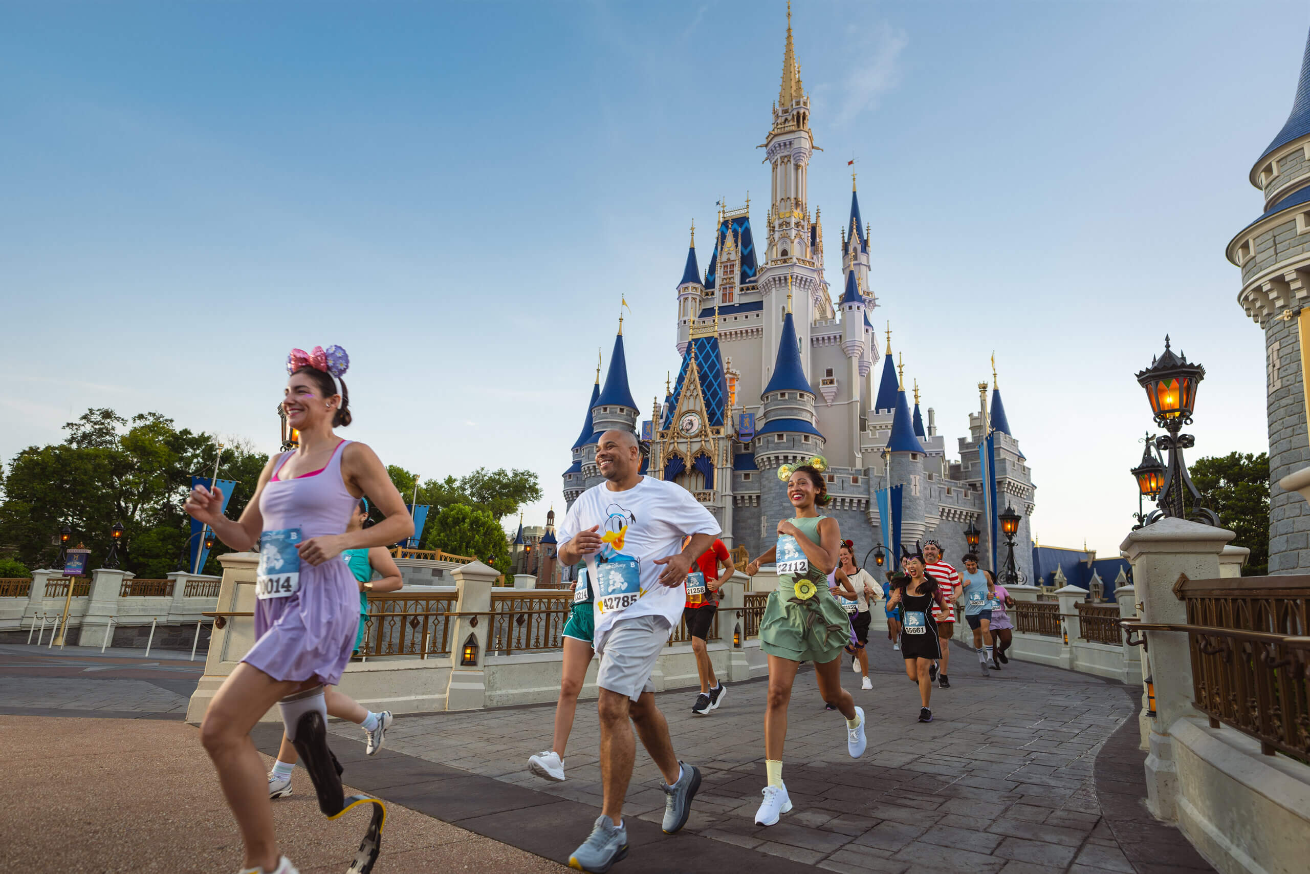 A group of people run past Cinderella Castle at Disney World on a sunny day, some wearing race bibs and costumes, all smiling and enjoying the event.