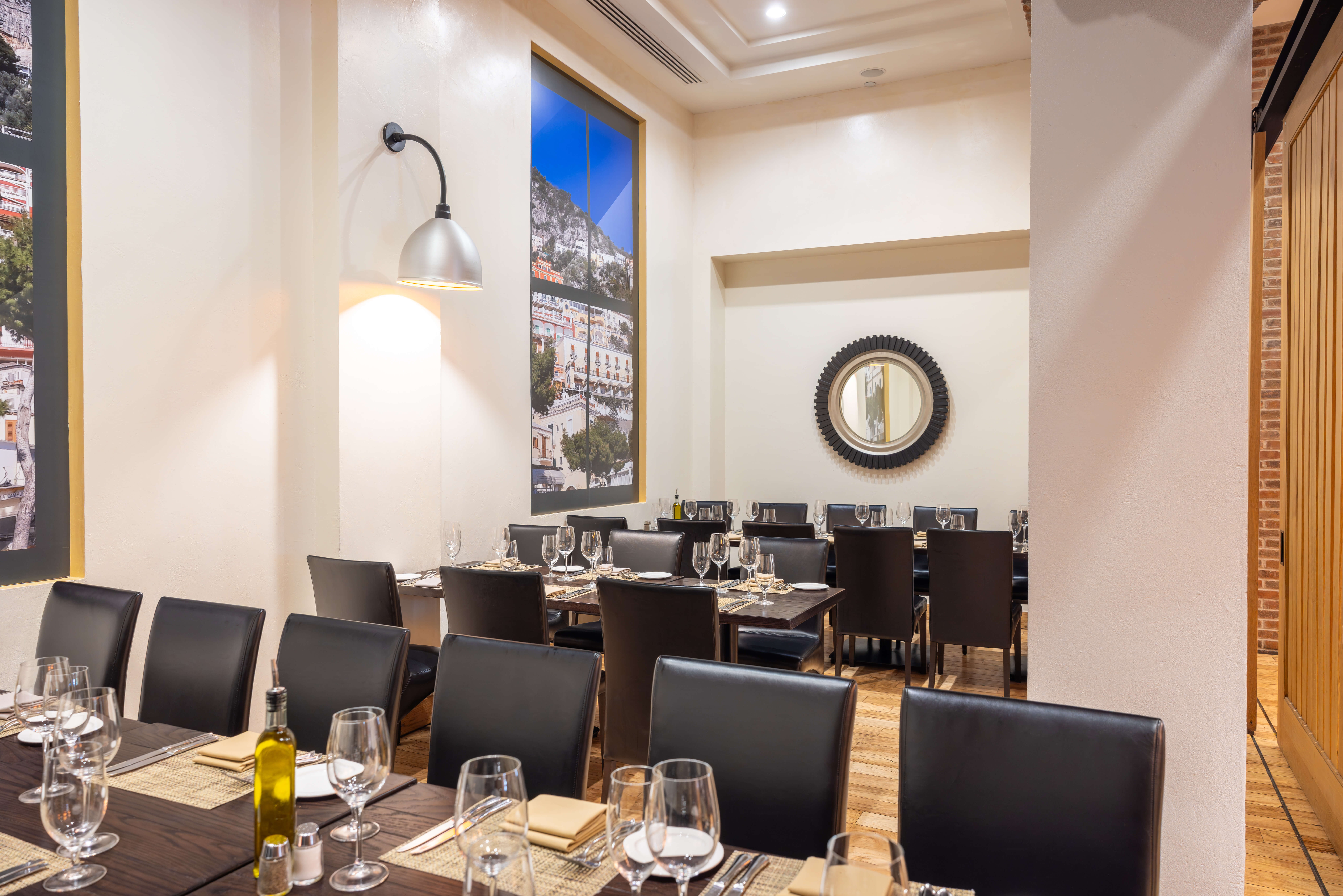 A dining room with long tables and chairs set for a private dining event, with place settings and olive oil on the table.