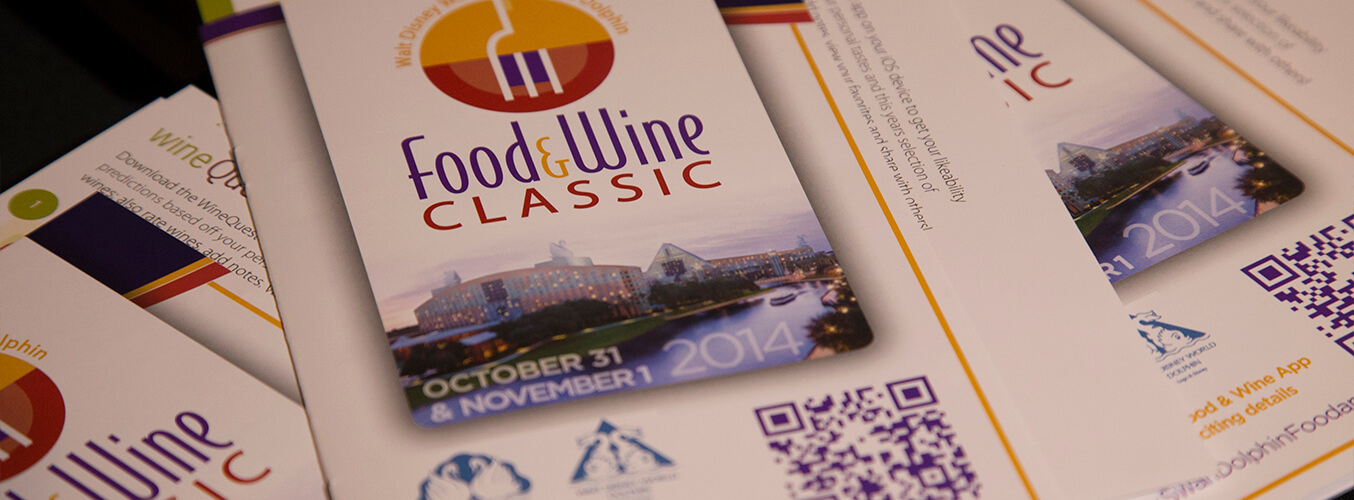 Close-up of brochures for the Food &amp; Wine Classic event, featuring colorful text and graphics, with the event dates October 31 and November 1, 2014, and an image of a cityscape at dusk.