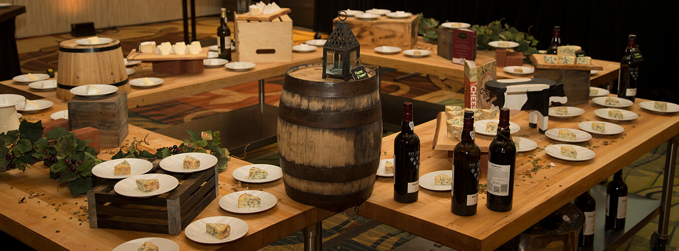 Un allestimento da tavolo con bottiglie di vino, vassoi di formaggi, botti decorative, cassette e elementi decorativi a tema viticolo, che crea un’ambientazione elegante per un evento di degustazione di vini e formaggi.