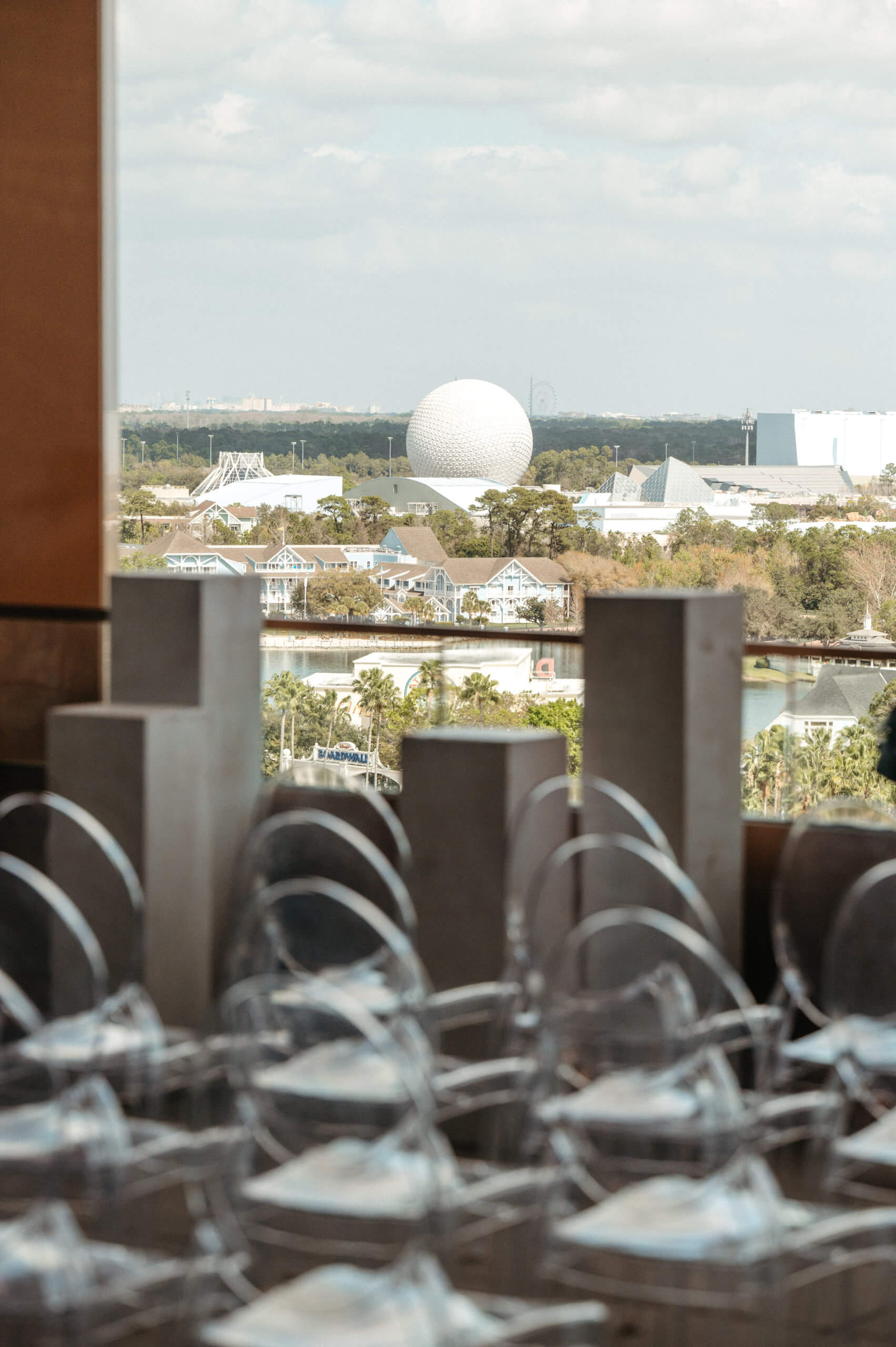 窓から見える景色。手前には透明な椅子がずらりと並び、背景にはWalt Disney World にあるエプコットの白いジオデシック・ドームが、木々やその他のパークの建物に囲まれて映っている。